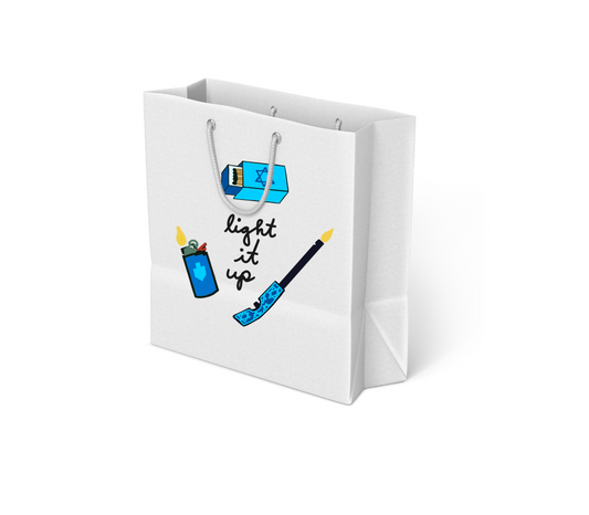 White gift bag with rope handles featuring illustrations of a blue lighter with a flame, a blue matchbox with a Star of David, and a blue candle holder, with the words “light it up” in black script