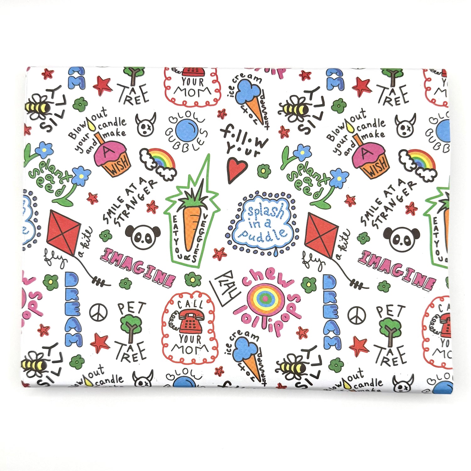 Colorful illustrated wrapping paper with playful doodles and phrases like 'Imagine,' 'Dream,' and 'Call Your Mom,' featuring a panda, kite, rainbow, and bumblebee on a white background