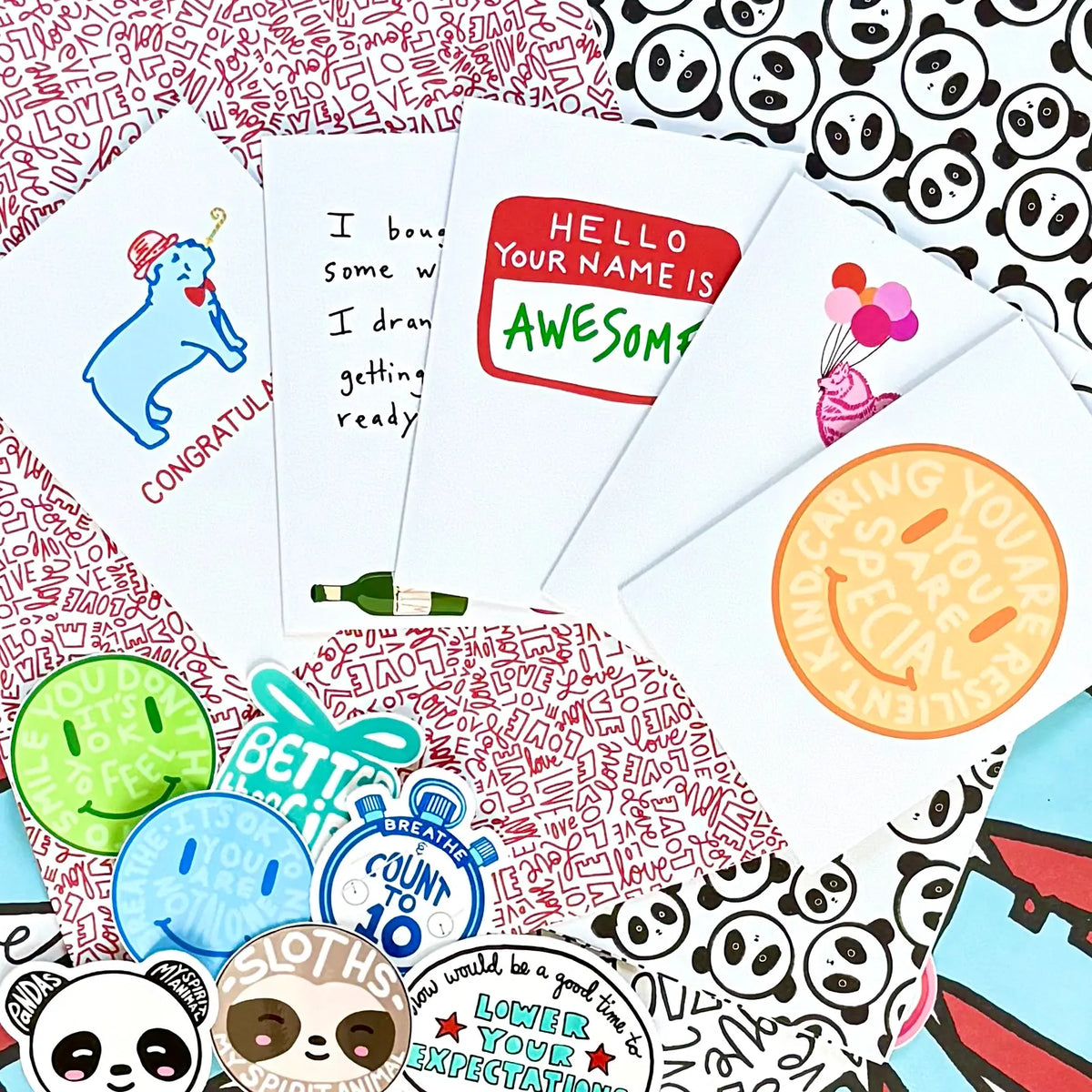 Assorted greeting cards and stickers arranged on a patterned background with repeating red and white ‘LOVE’ text.