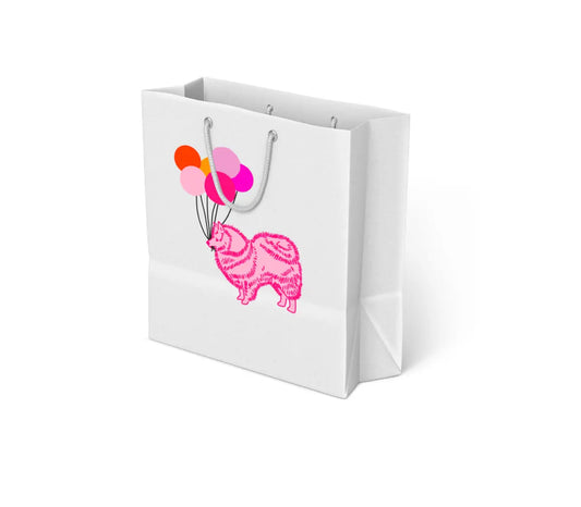 White gift bag with gray rope handles featuring an illustration of a pink dog holding five colorful balloons in its mouth