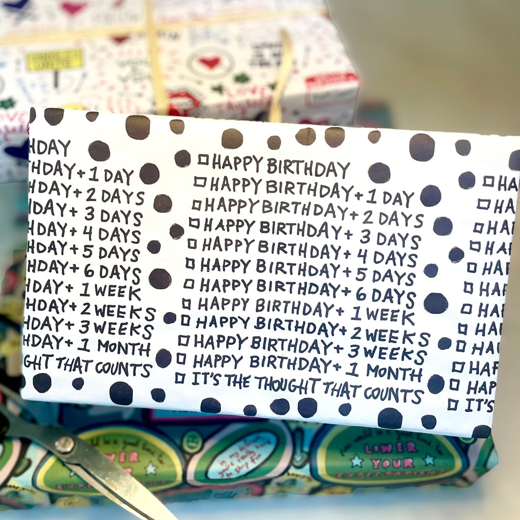 Gift wrap adorned in white paper with black font showing a checklist of different boxes you can check for how late you are in wishing Happy Birthday, like Happy Birthday plus one day, happy birthday plus tow days in handwritten font. The last checked box says, 